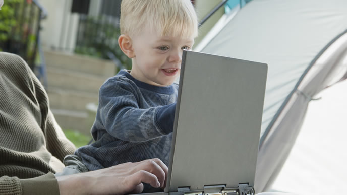 キャンプ先で仕事中のパパのパソコンを見る赤ちゃん