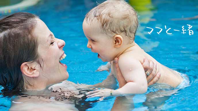 プールの中でママに掴んでもらう笑顔の赤ちゃん