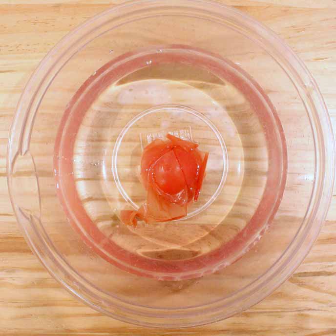 ボウルの中の熱湯に入れられ、皮が剥がれてきたトマト