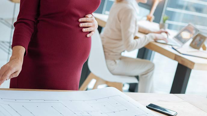 職場のデスクの前に立つ妊婦
