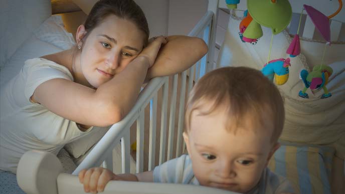 寝付かない赤ちゃんを虚ろな目で見つめる母親