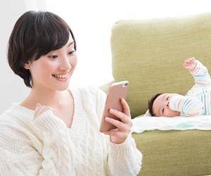 赤ちゃんの傍でスマホを見て笑顔の母親