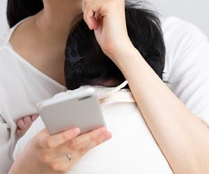 赤ちゃんの授乳中にスマホを見つめる女性